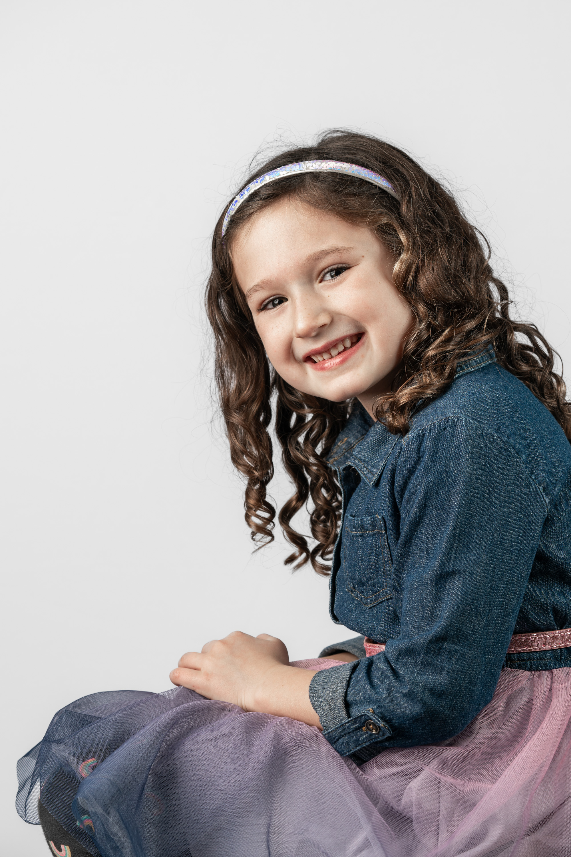 a curly hair girl playfully smiles in her frilly dress