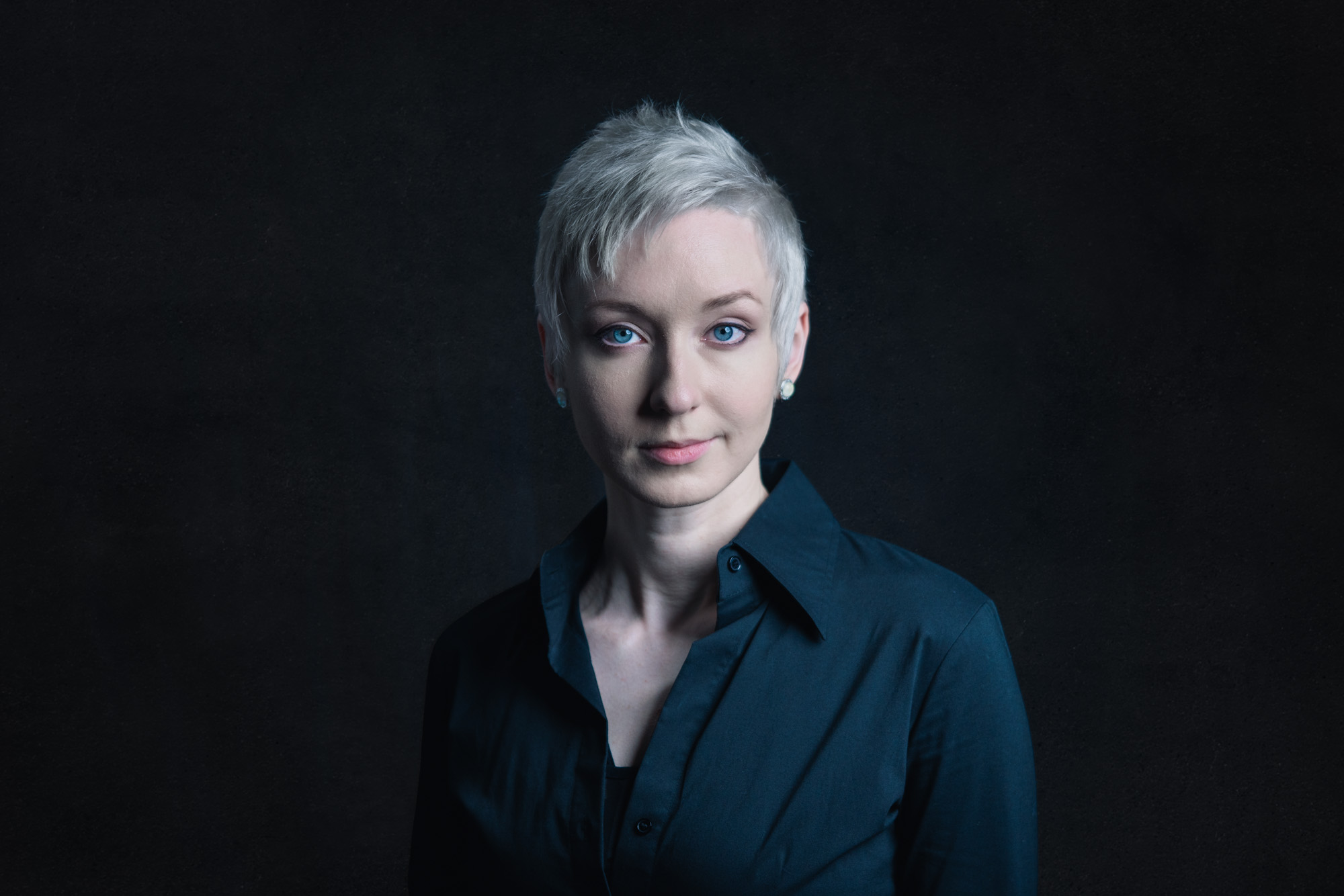 a short haired woman stares into the camera in a black dress shirt