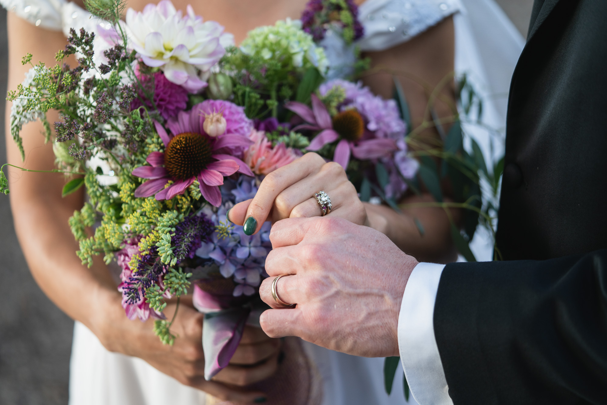 a bride holds her bouquet while she and the groom show their rings